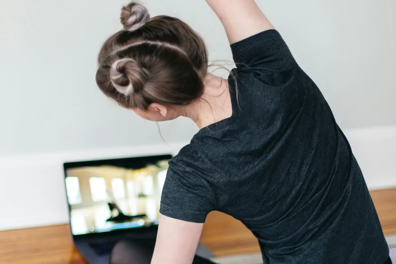 Person auf einer Yogamatte in einer Seitdehnung vor einem aufgeklappten Laptop