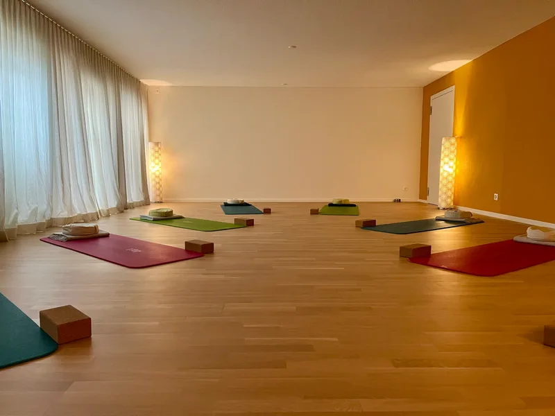Blick in den Yogaraum mit ausgelegten Matten vor der ockergelben Wand